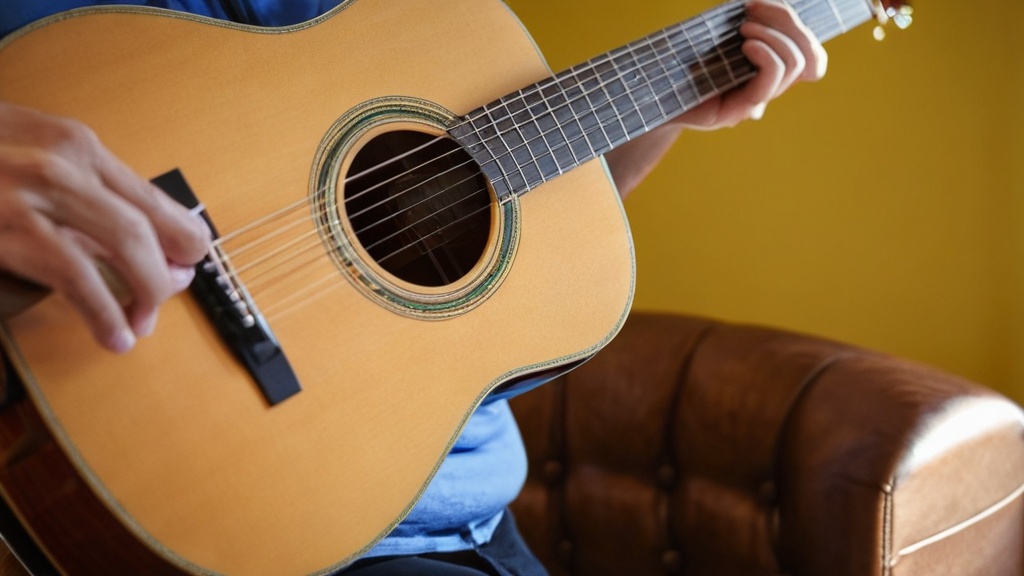 Persoon speelt akoestische gitaar, zittend op een leren bank